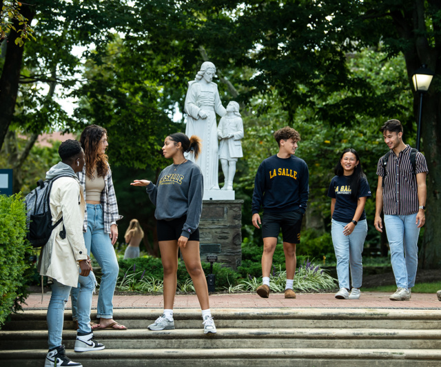 Groups of students walking and talking together with St. Joh Baptist de La Salle statue in the background.