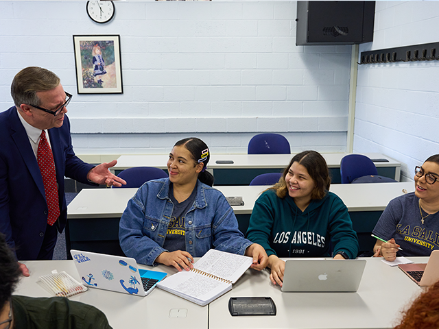 Image of a professor speaking to three students in a classroom