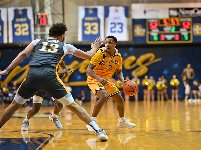 A basketball player dribbling the ball with two defenders following him