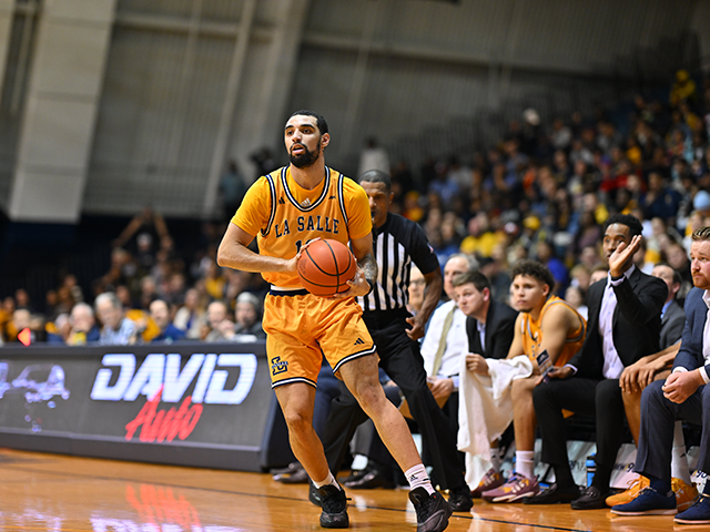 A men's basketball player holding the ball and looking at his teammates