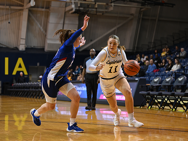 A women's basketball player dribbling the ball as her opponent follows.