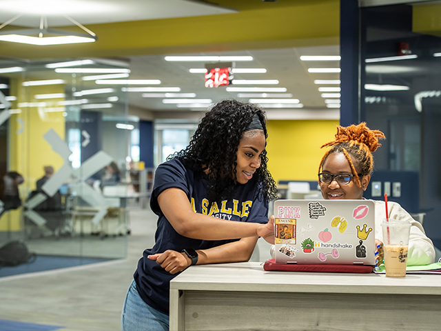Image of two female students working on a laptop in the library.