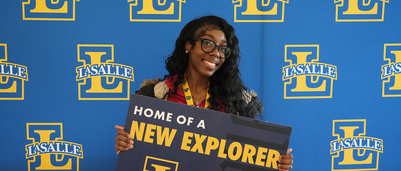 Image of a new student holding a "Home of a New Explorer" lawn sign.