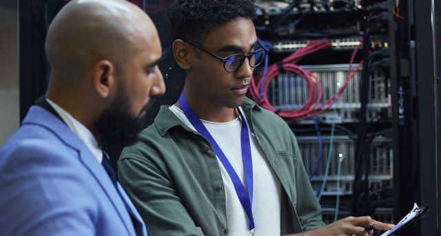 Cropped shot of two male IT support agents working together in a dark network server room.