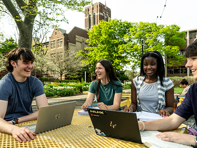 4 students sitting at a table on the Quad and laughing