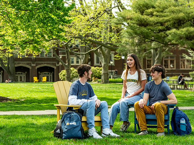 Image of 3 students sitting on the Quad and chatting